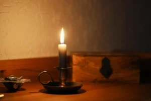 Image shows a lit wax candle on wooden a table, with a wall in the background, and depicts the history of scented candles being used throughout the ages.