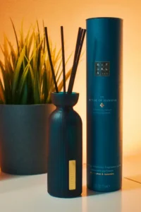 Picture of a scented reed diffuser on a table next to its packaging. In the background is a plant in a pot.
