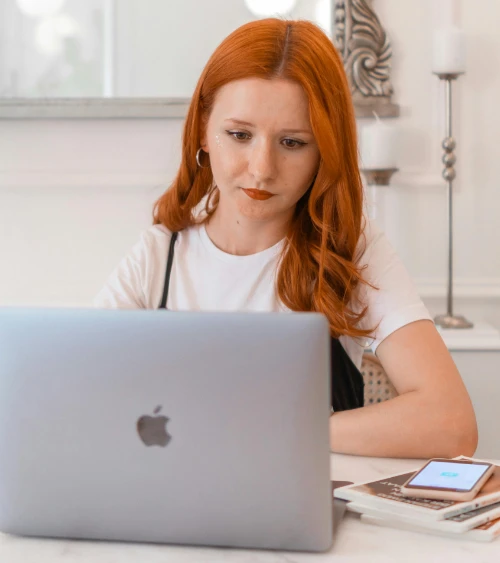 A woman stares intently at her laptop PC, concentrating on writing her candle making business plan. Her mobile phone rests on top of three books, each about how to start a candle making business.